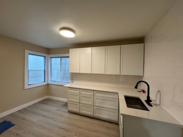 kitchen featuring tasteful backsplash, light countertops, a sink, light wood-type flooring, and baseboards