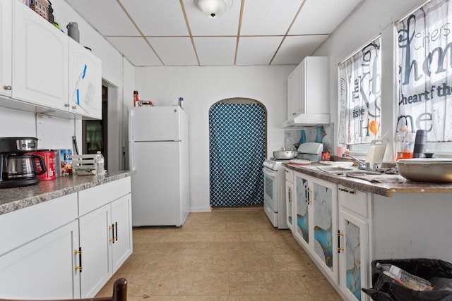 kitchen featuring a drop ceiling, white appliances, white cabinetry, and a sink