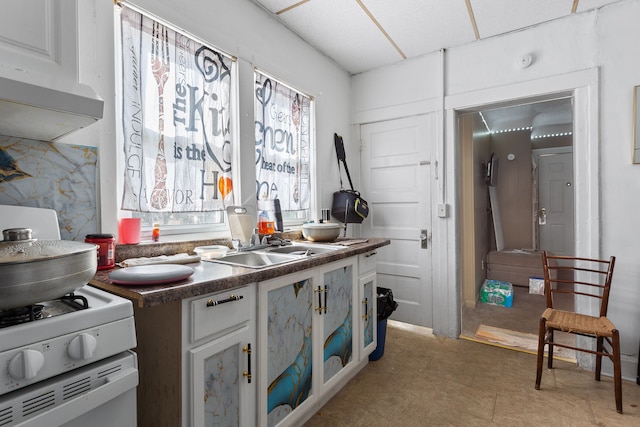 kitchen with a sink, a drop ceiling, gas range gas stove, dark countertops, and white cabinets