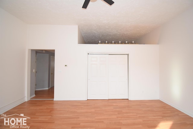 unfurnished bedroom featuring lofted ceiling, a closet, a textured ceiling, and wood finished floors