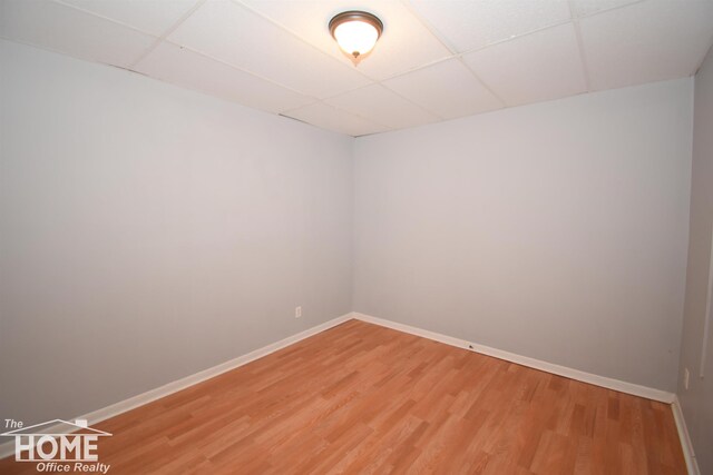 spare room with baseboards, a paneled ceiling, and light wood-style floors