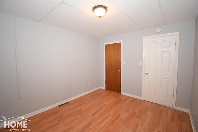 unfurnished room featuring light wood finished floors, a drop ceiling, visible vents, and baseboards