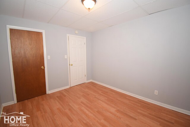 unfurnished bedroom with a paneled ceiling, baseboards, and light wood finished floors