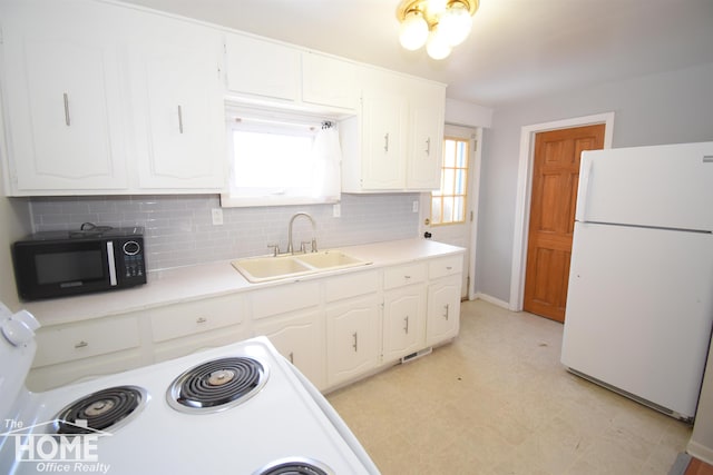 kitchen featuring black microwave, a sink, white cabinets, freestanding refrigerator, and light floors