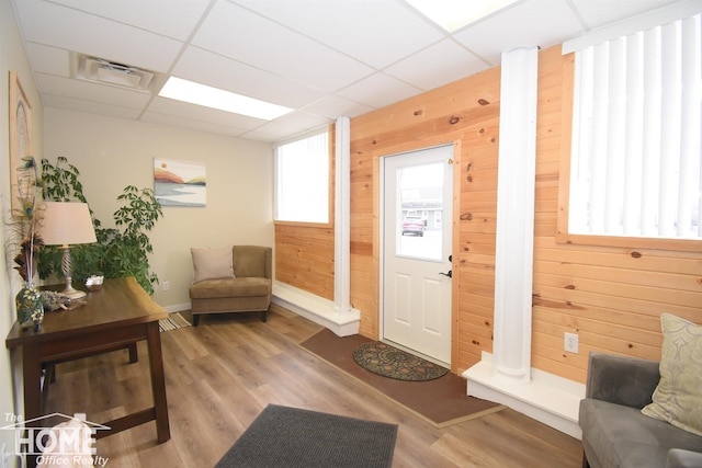 interior space featuring a drop ceiling, wooden walls, wood finished floors, visible vents, and ornate columns