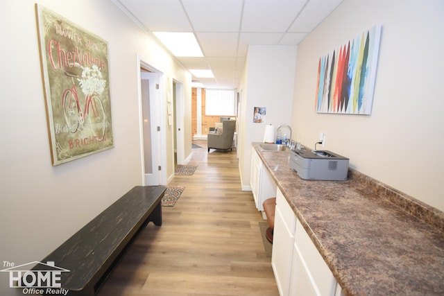 hall featuring a drop ceiling, a sink, light wood-style flooring, and baseboards