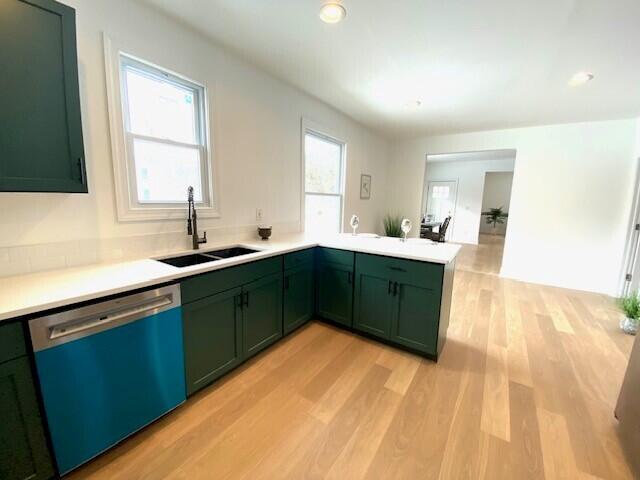 kitchen with dishwashing machine, light wood-style flooring, a peninsula, green cabinets, and a sink