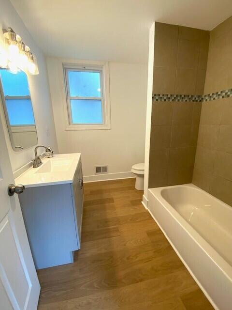 bathroom with toilet, wood finished floors, vanity, visible vents, and baseboards