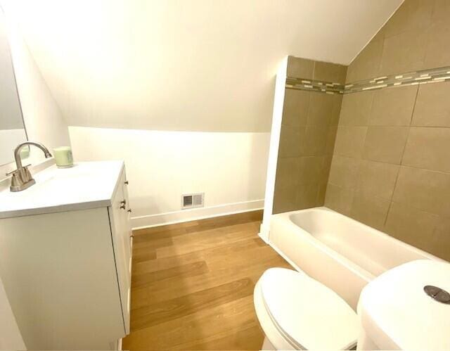 bathroom featuring visible vents, toilet, wood finished floors, vaulted ceiling, and vanity