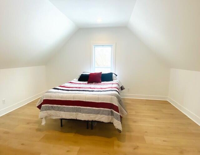 bedroom featuring lofted ceiling, baseboards, and wood finished floors