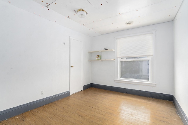 spare room with wood finished floors, visible vents, and baseboards