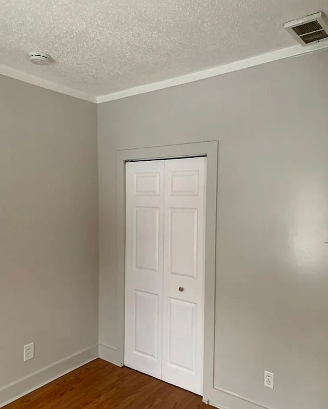 unfurnished bedroom with visible vents, a textured ceiling, dark wood-style floors, a closet, and baseboards