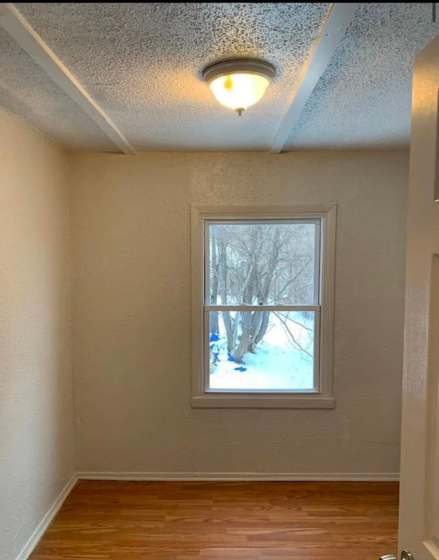 empty room featuring wood finished floors, baseboards, a textured wall, and a textured ceiling