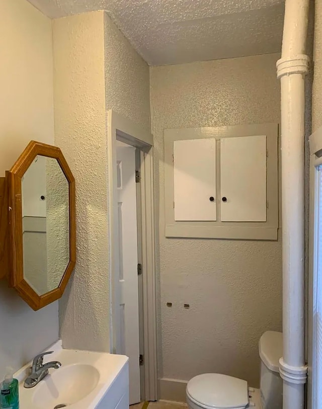 half bath featuring a sink, toilet, a textured ceiling, and a textured wall