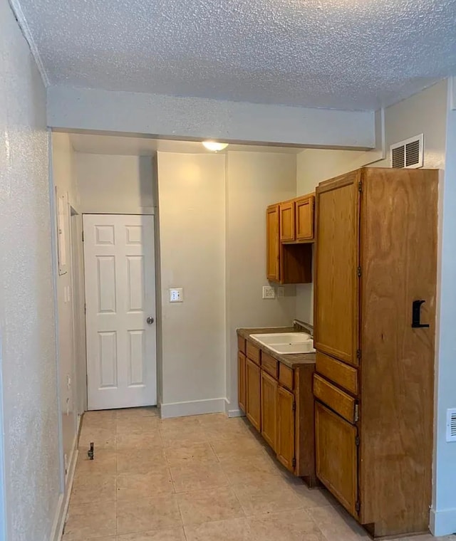 kitchen with brown cabinetry, baseboards, visible vents, a sink, and a textured ceiling