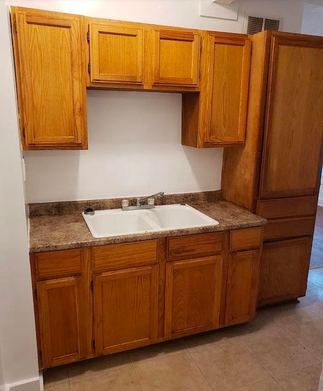 kitchen with dark countertops, brown cabinetry, visible vents, and a sink