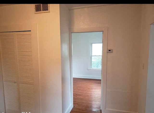 hall with a textured wall, visible vents, baseboards, and wood finished floors