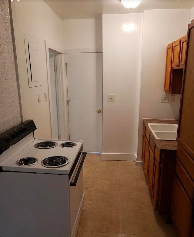 kitchen featuring light tile patterned floors, brown cabinetry, baseboards, electric range, and a sink