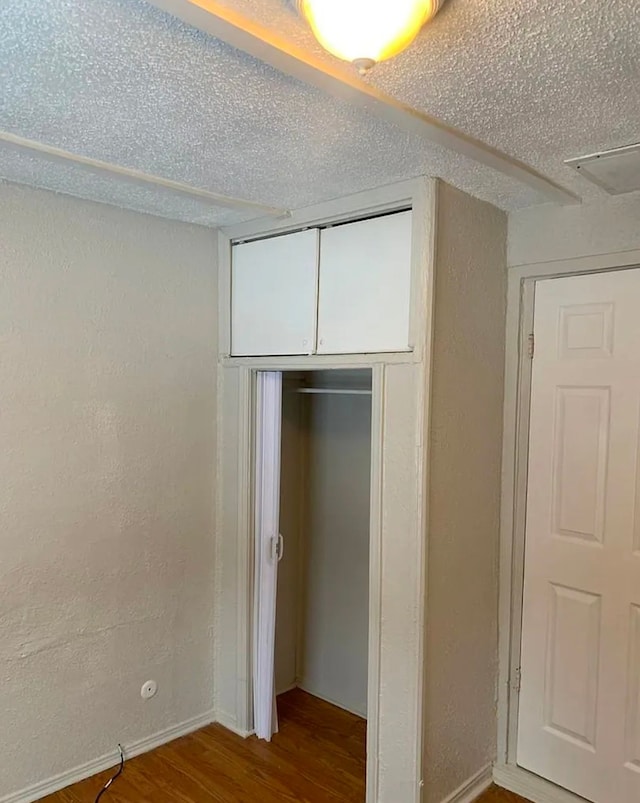 unfurnished bedroom featuring wood finished floors, a closet, a textured wall, and a textured ceiling