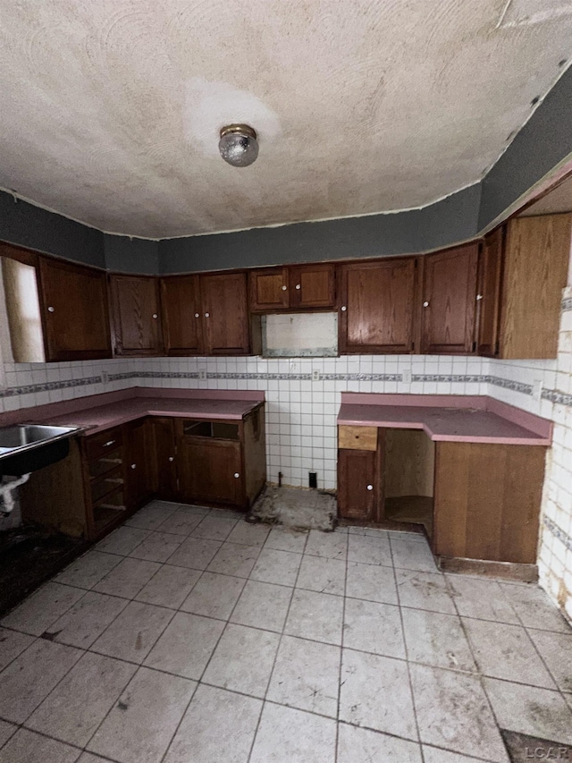 kitchen featuring a textured ceiling, light tile patterned floors, a sink, and tile walls