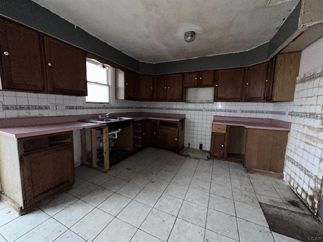 kitchen featuring a textured ceiling, light tile patterned flooring, dark brown cabinetry, a sink, and backsplash