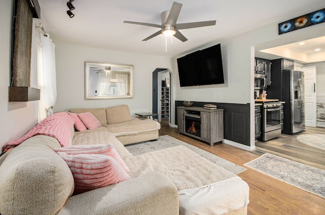 living area featuring light wood-type flooring, a fireplace, arched walkways, and ceiling fan