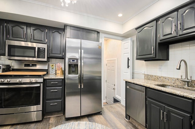 kitchen featuring decorative backsplash, ornamental molding, wood finished floors, stainless steel appliances, and a sink