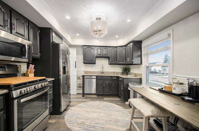 kitchen featuring light wood finished floors, tasteful backsplash, ornamental molding, stainless steel appliances, and a chandelier