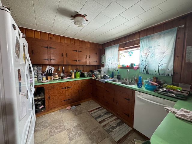 kitchen with white appliances, wooden walls, brown cabinetry, and a sink