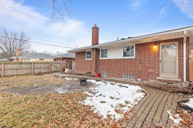 back of house with brick siding, a chimney, a gate, fence, and a fire pit