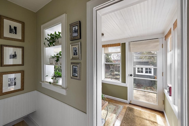 doorway to outside with light wood-type flooring and wainscoting