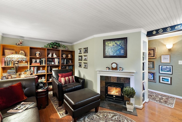 living area with a tile fireplace, crown molding, baseboards, and wood finished floors