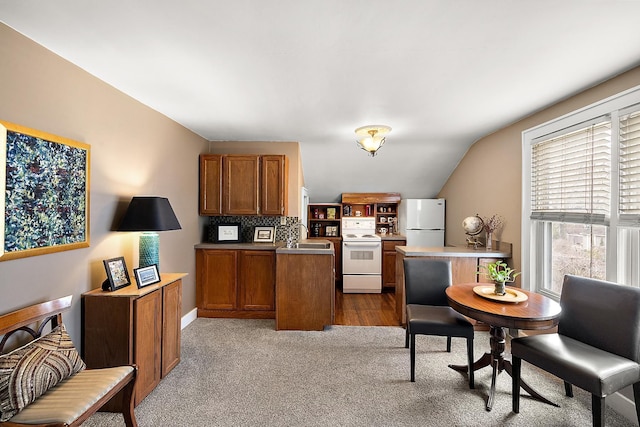 kitchen with white appliances, carpet flooring, a sink, vaulted ceiling, and brown cabinetry