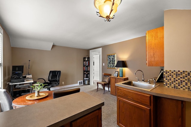 kitchen featuring light carpet, a sink, visible vents, backsplash, and brown cabinetry