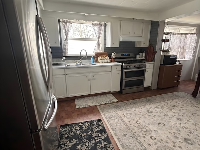 kitchen with under cabinet range hood, white cabinetry, appliances with stainless steel finishes, and a sink