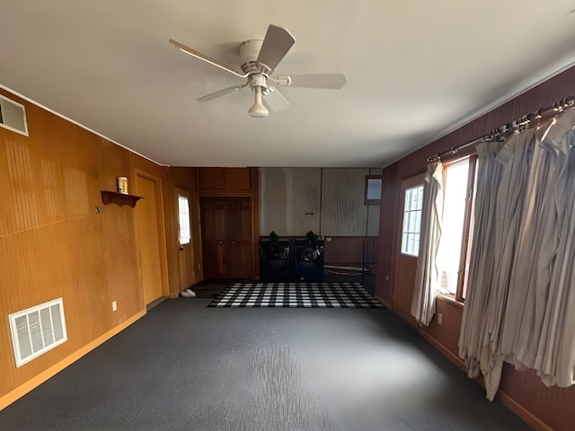 empty room with ceiling fan, baseboards, visible vents, and wooden walls