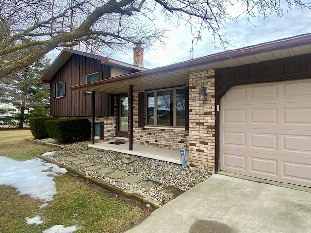 view of front facade featuring a garage, a chimney, board and batten siding, and brick siding