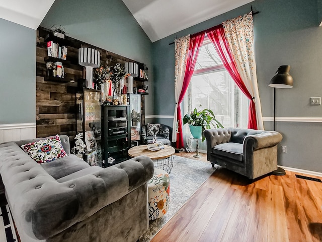 living area with visible vents, wainscoting, lofted ceiling, and wood finished floors