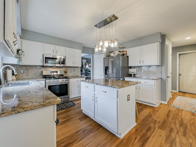 kitchen featuring light wood-type flooring, light stone counters, white cabinets, stainless steel appliances, and a sink