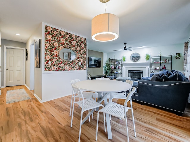 dining room featuring a ceiling fan, a fireplace, and light wood finished floors