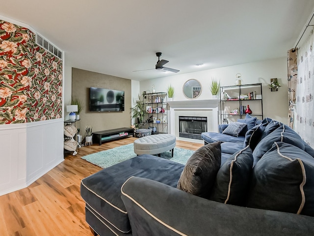 living area featuring a wainscoted wall, a fireplace, ceiling fan, and wood finished floors