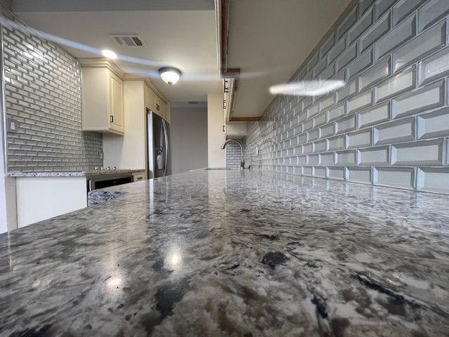 kitchen featuring a sink, visible vents, backsplash, stainless steel refrigerator, and light stone countertops