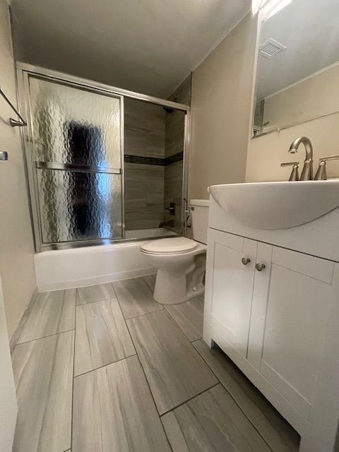 bathroom featuring toilet, shower / bath combination with glass door, visible vents, and vanity