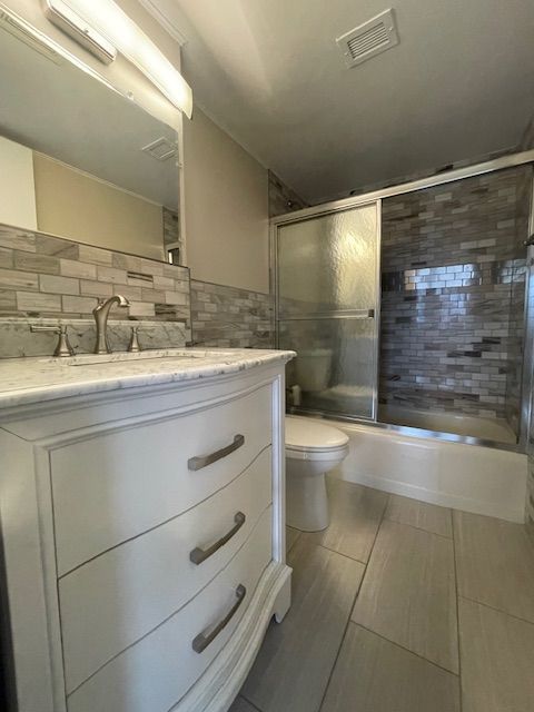 bathroom with visible vents, backsplash, toilet, combined bath / shower with glass door, and vanity