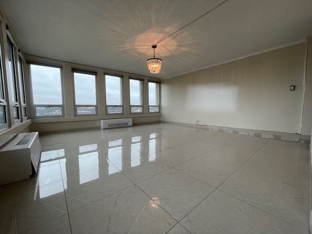 spare room with a chandelier, radiator heating unit, tile patterned flooring, and baseboards