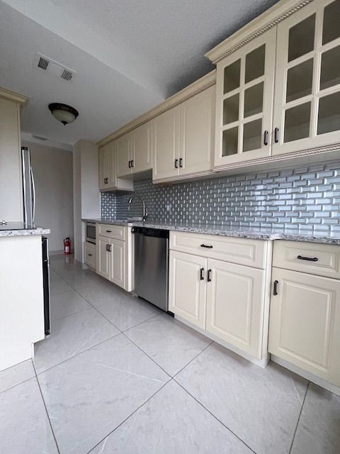 kitchen featuring light stone counters, visible vents, backsplash, appliances with stainless steel finishes, and glass insert cabinets