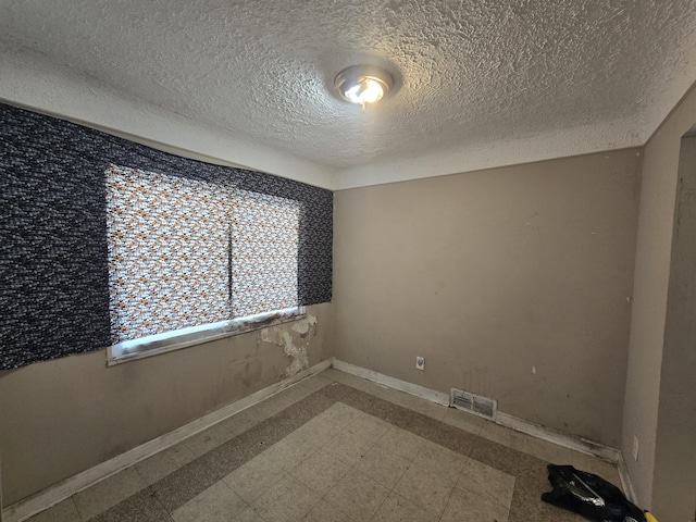 spare room with visible vents, a textured ceiling, baseboards, and tile patterned floors