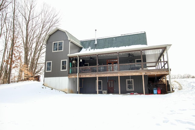 snow covered back of property with a gambrel roof, a wooden deck, and a ceiling fan