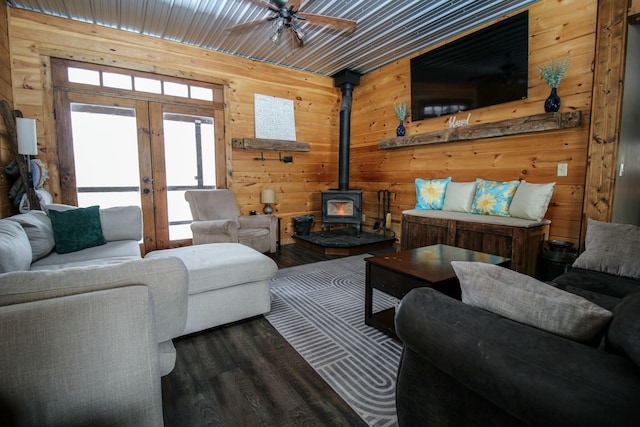 living area featuring french doors, a ceiling fan, a wood stove, wooden walls, and wood finished floors