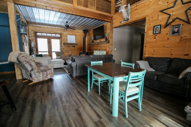 dining space with a ceiling fan, wood finished floors, a wood stove, french doors, and wood walls